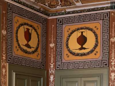 Le pareti laterali, delimitate da due porte verdi sovrastate da grandi riquadri con anfore scure...